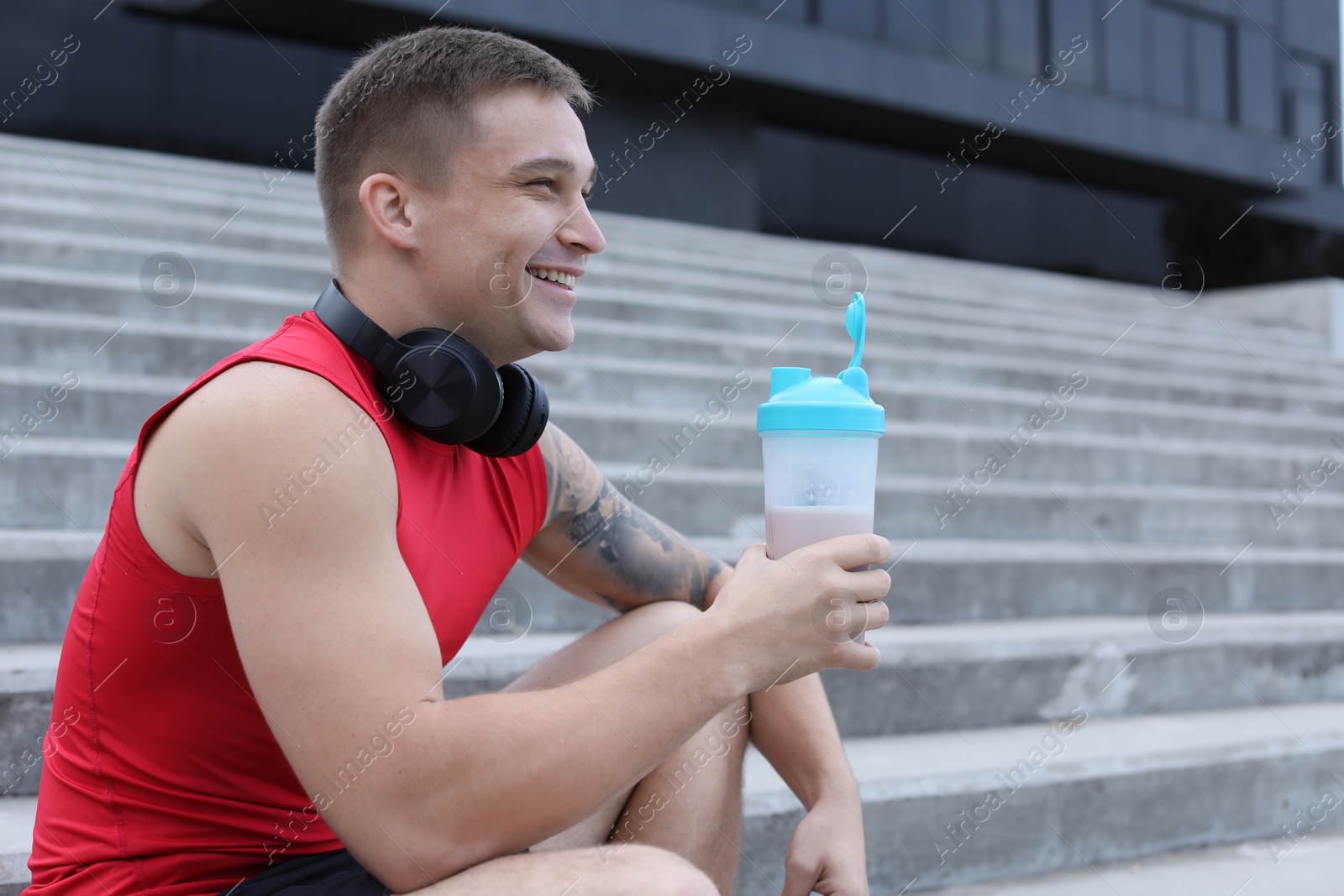 Photo of Smiling man with shaker of protein drink outdoors. Space for text