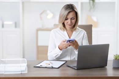 Photo of Businesswoman using smartphone at table in office