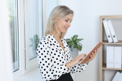 Photo of Happy businesswoman using tablet near window in office