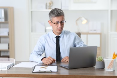 Photo of Businessman working with laptop at table in office