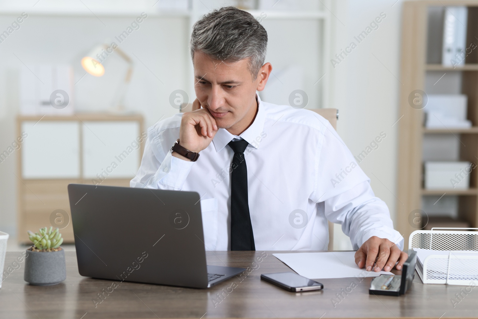 Photo of Businessman working with laptop at table in office