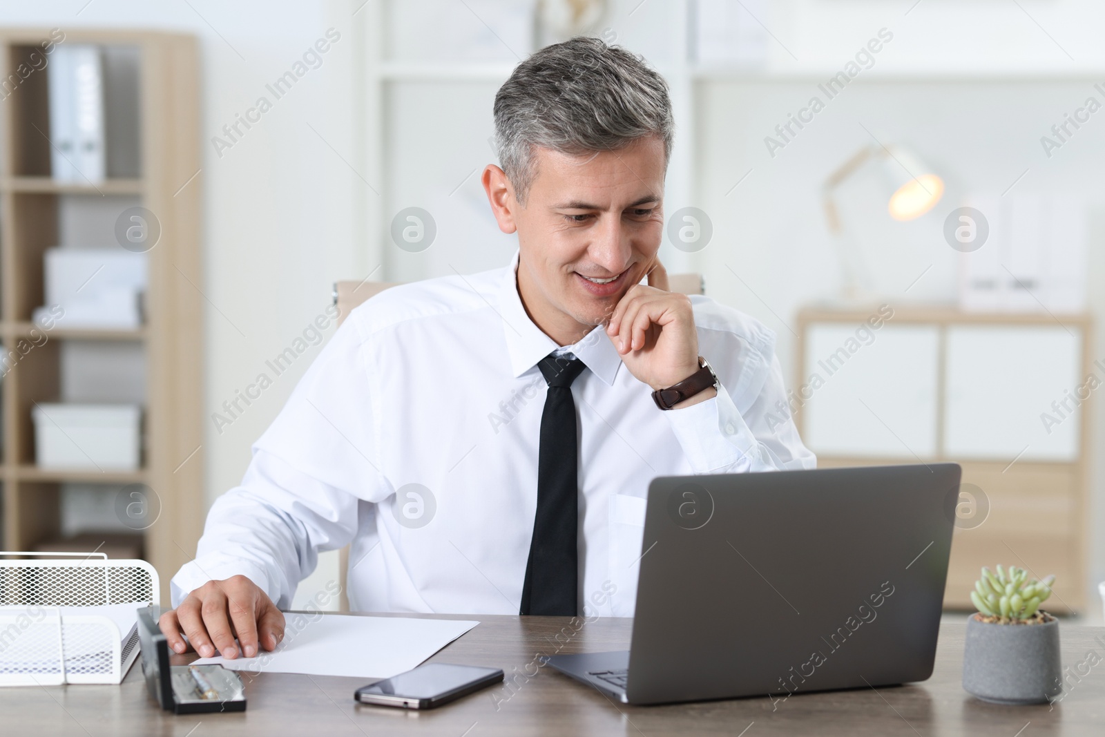 Photo of Businessman working with laptop at table in office