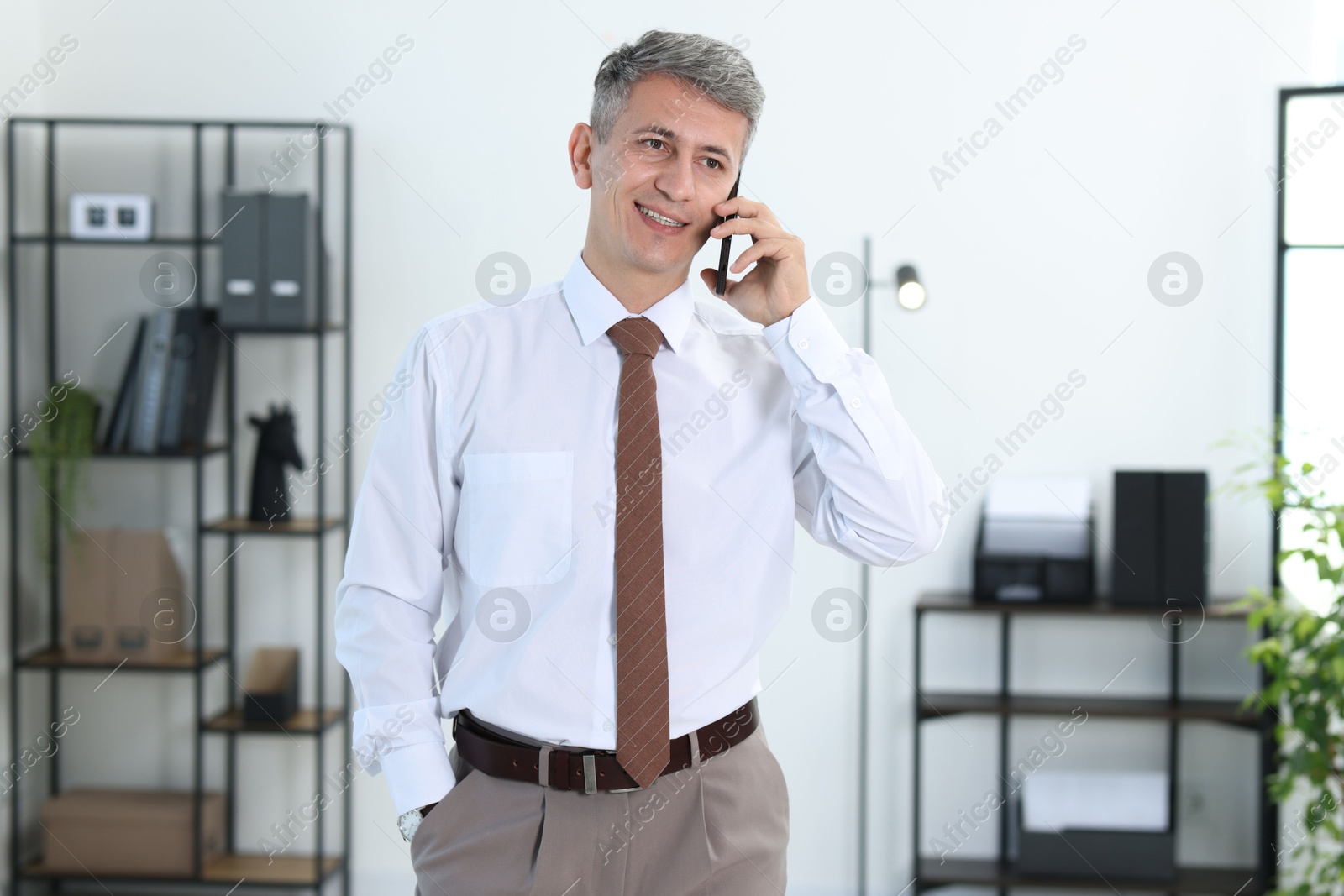 Photo of Happy businessman talking on smartphone in office