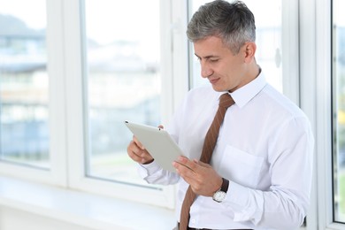 Photo of Businessman using tablet near window in office, space for text