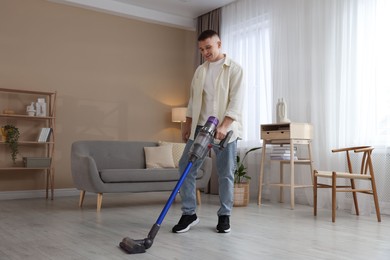 Photo of Young man cleaning floor with cordless vacuum cleaner at home