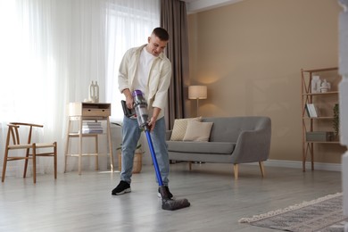 Photo of Young man cleaning floor with cordless vacuum cleaner at home