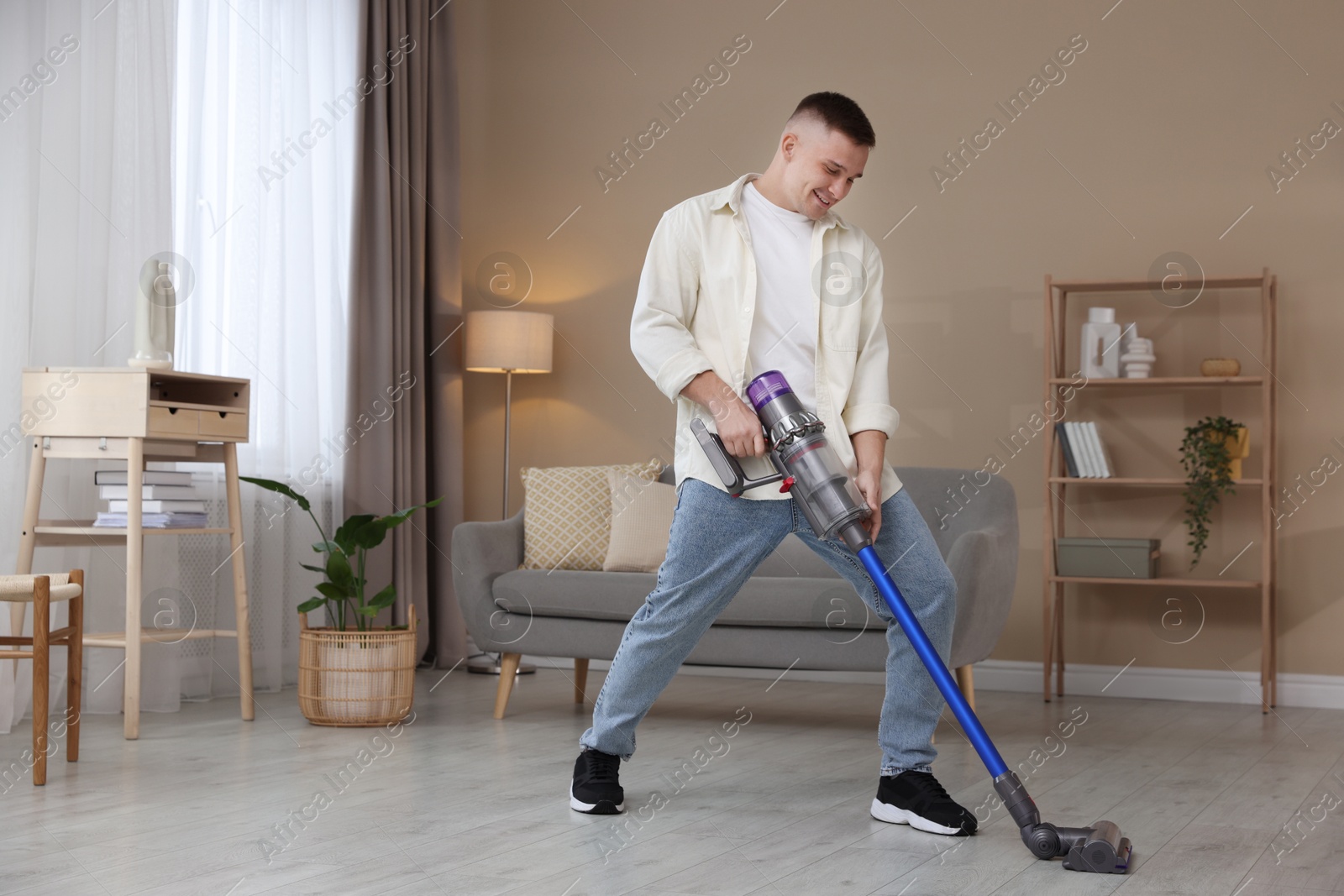 Photo of Young man cleaning floor with cordless vacuum cleaner at home