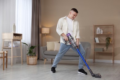 Photo of Young man cleaning floor with cordless vacuum cleaner at home