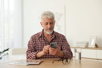 Photo of Senior man using smartphone at table indoors