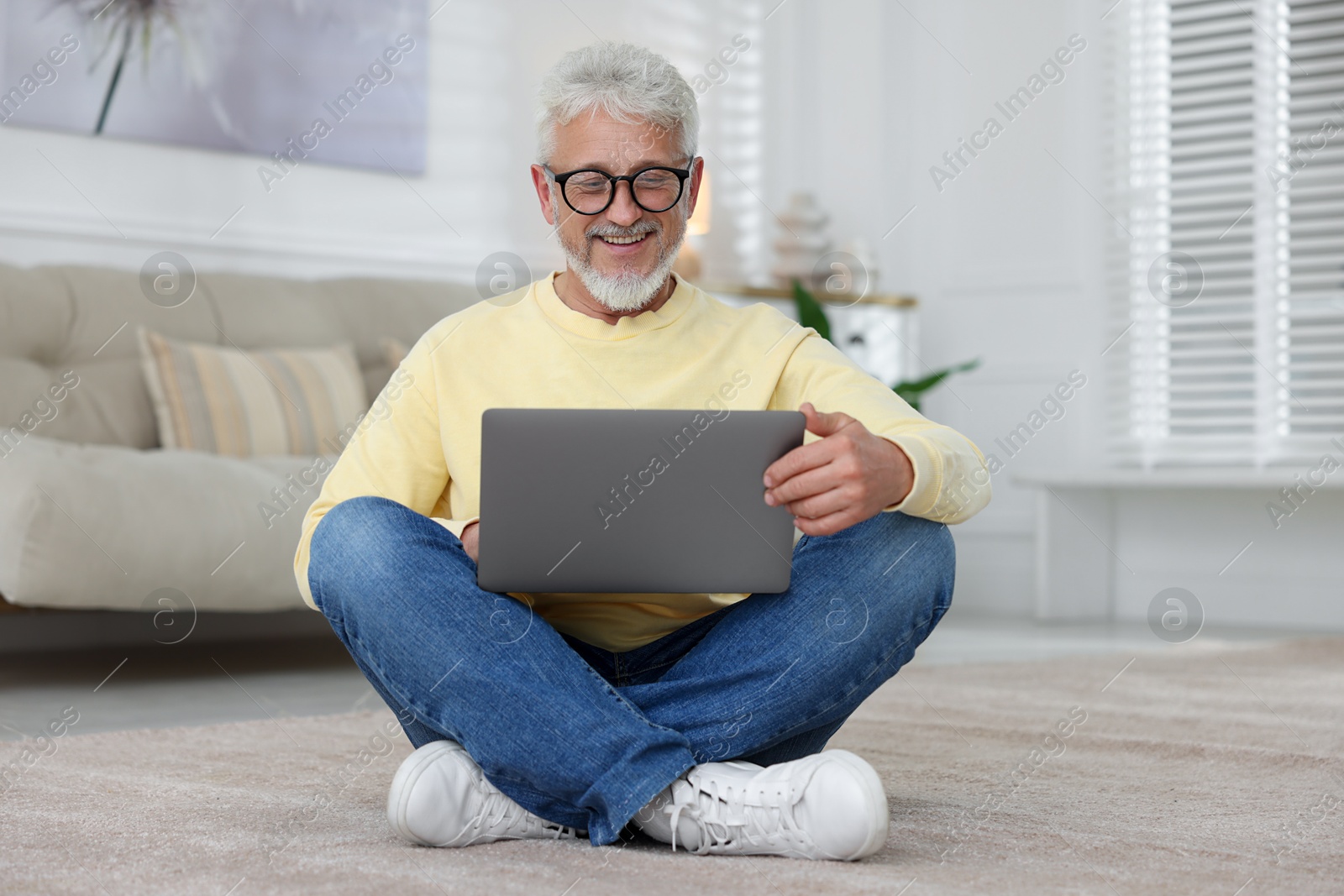 Photo of Senior man using laptop on floor at home