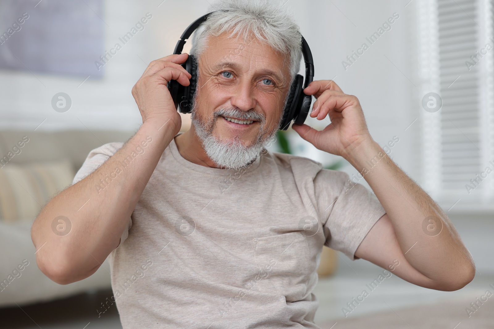 Photo of Smiling senior man in headphones listening to music at home