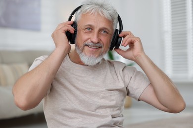 Photo of Smiling senior man in headphones listening to music at home