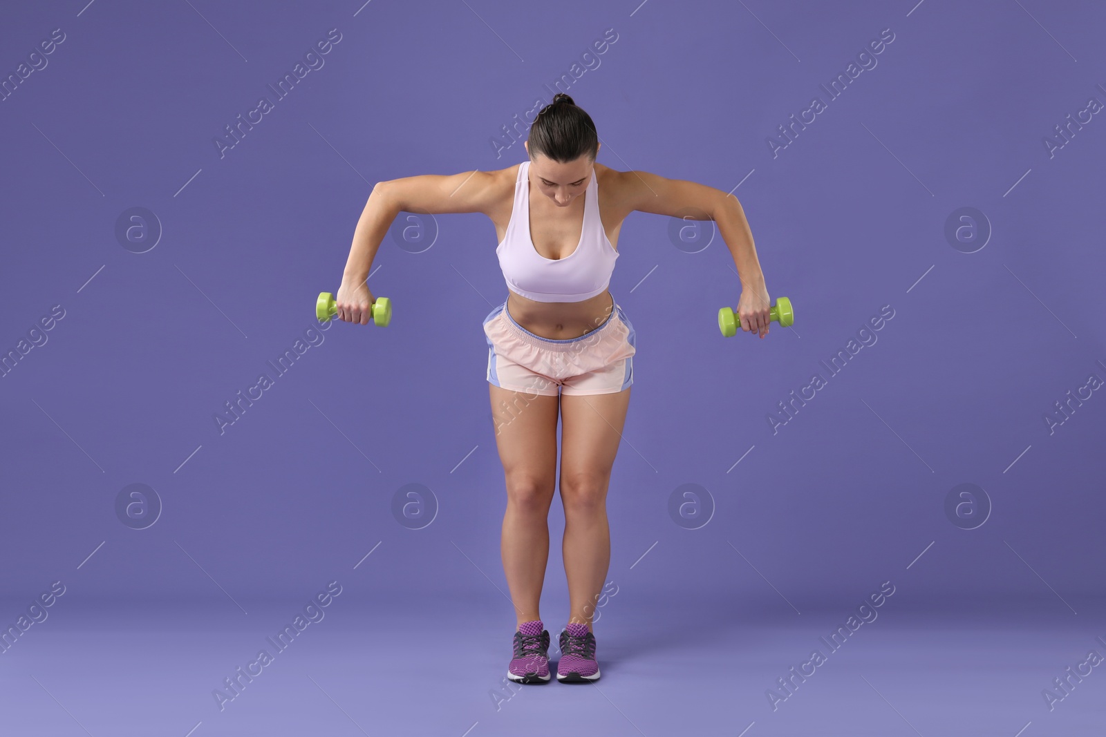 Photo of Woman exercising with dumbbells on purple background