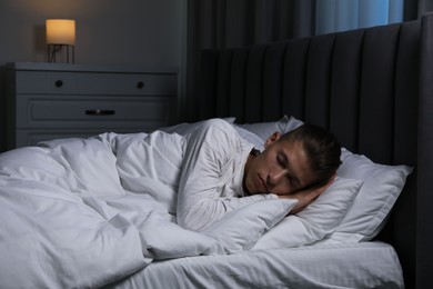 Photo of Young man sleeping in soft bed at night