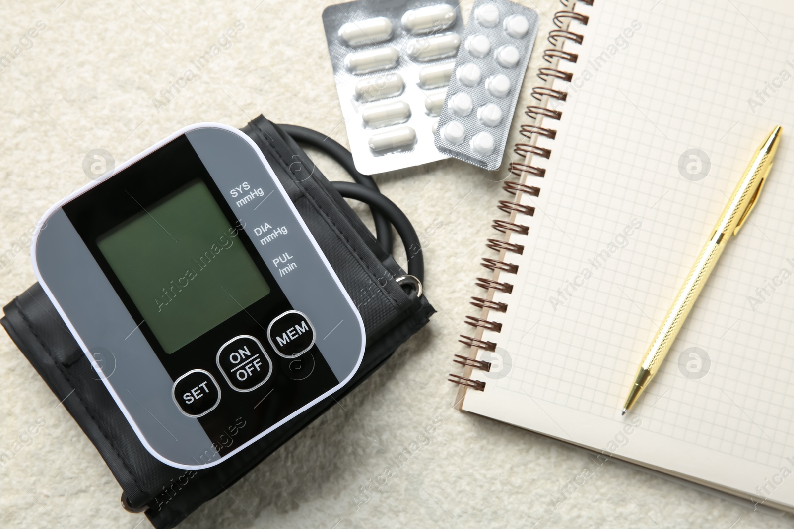 Photo of Blood pressure measuring device, pills and notebook on light textured background, top view