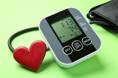 Photo of Blood pressure measuring device and heart figure on green background, closeup