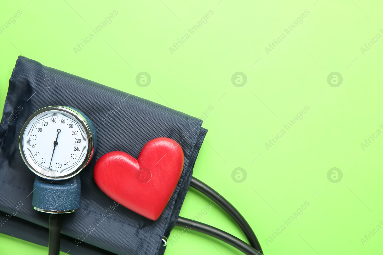 Photo of Blood pressure measuring device and heart figure on green background, top view. Space for text