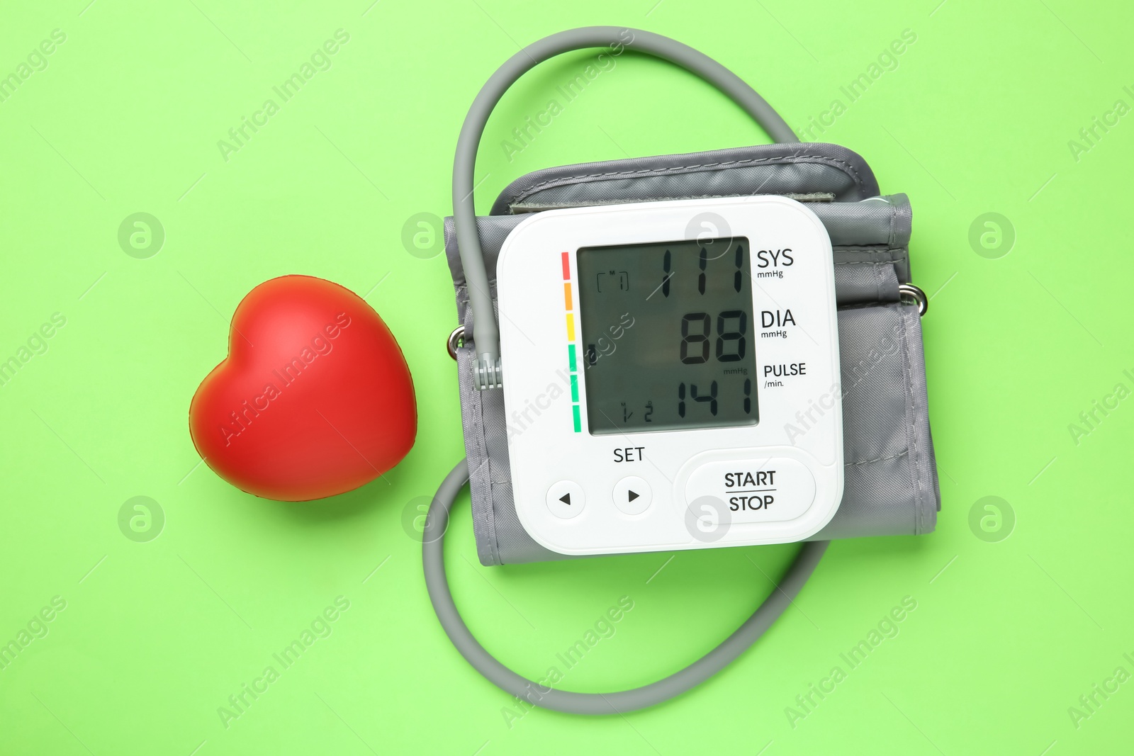 Photo of Blood pressure measuring device and squeeze heart on green background, top view