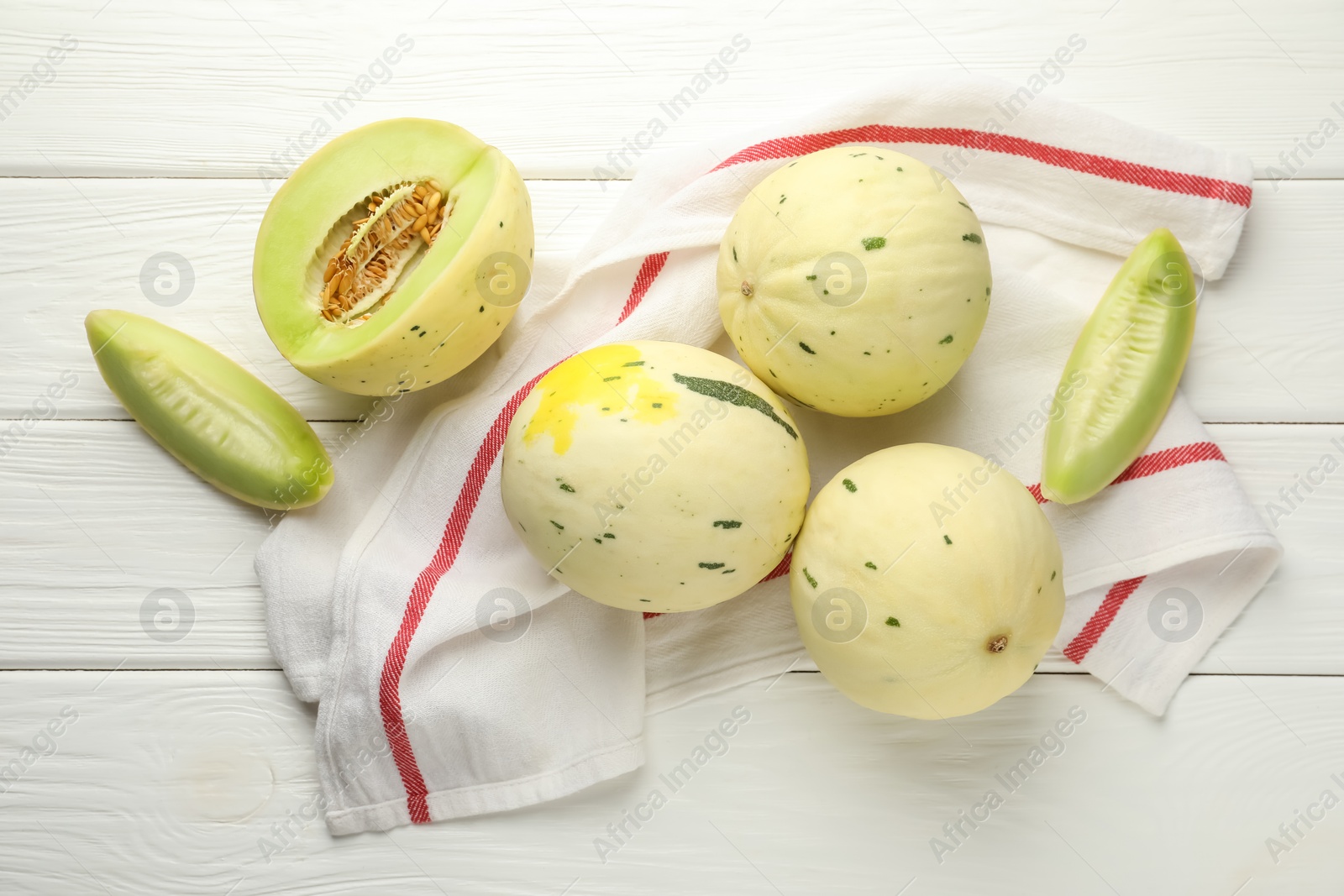 Photo of Fresh whole and cut honeydew melons on white wooden table, flat lay