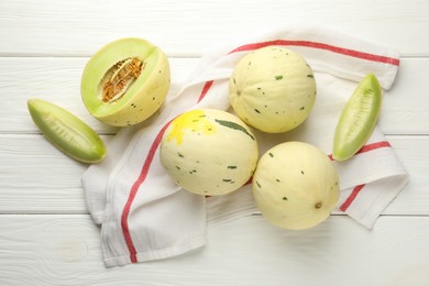 Photo of Fresh whole and cut honeydew melons on white wooden table, flat lay