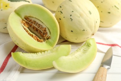 Photo of Fresh whole and cut honeydew melons on white wooden table, closeup