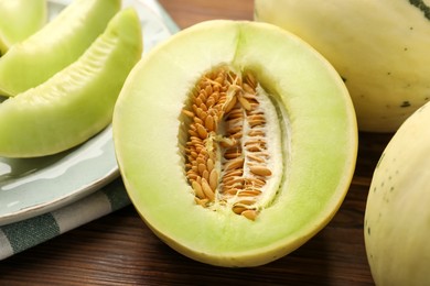 Photo of Fresh whole and cut honeydew melons on wooden table, closeup