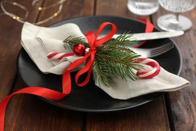 Photo of Christmas setting with plate, cutlery, fir branches and ribbon on wooden table, closeup