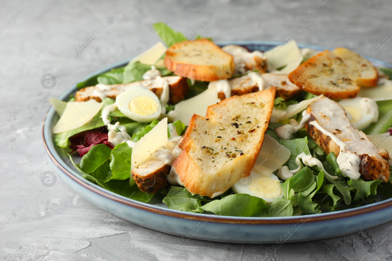 Photo of Tasty Caesar salad with chicken on gray textured table, closeup