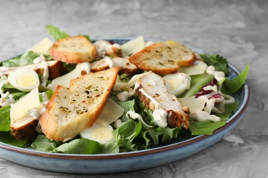 Photo of Tasty Caesar salad with chicken on gray textured table, closeup