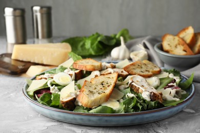 Photo of Tasty Caesar salad with chicken on gray textured table, closeup