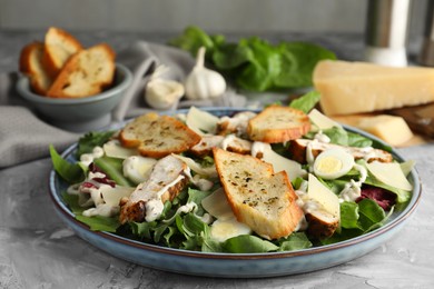 Photo of Tasty Caesar salad with chicken on gray textured table, closeup