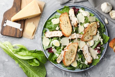 Photo of Tasty Caesar salad with chicken and ingredients on gray textured table, flat lay