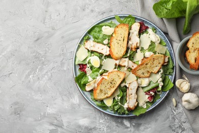 Photo of Tasty Caesar salad with chicken and ingredients on gray textured table, flat lay. Space for text