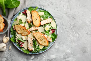 Photo of Tasty Caesar salad with chicken and ingredients on gray textured table, flat lay. Space for text