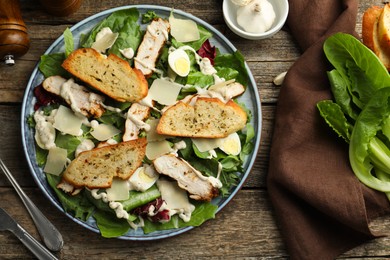 Photo of Tasty Caesar salad with chicken served on wooden table, flat lay