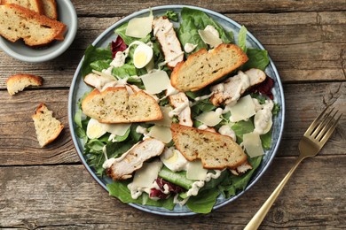 Photo of Tasty Caesar salad with chicken served on wooden table, flat lay