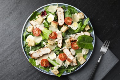 Photo of Tasty Caesar salad with chicken and tomatoes served on dark gray textured table, flat lay