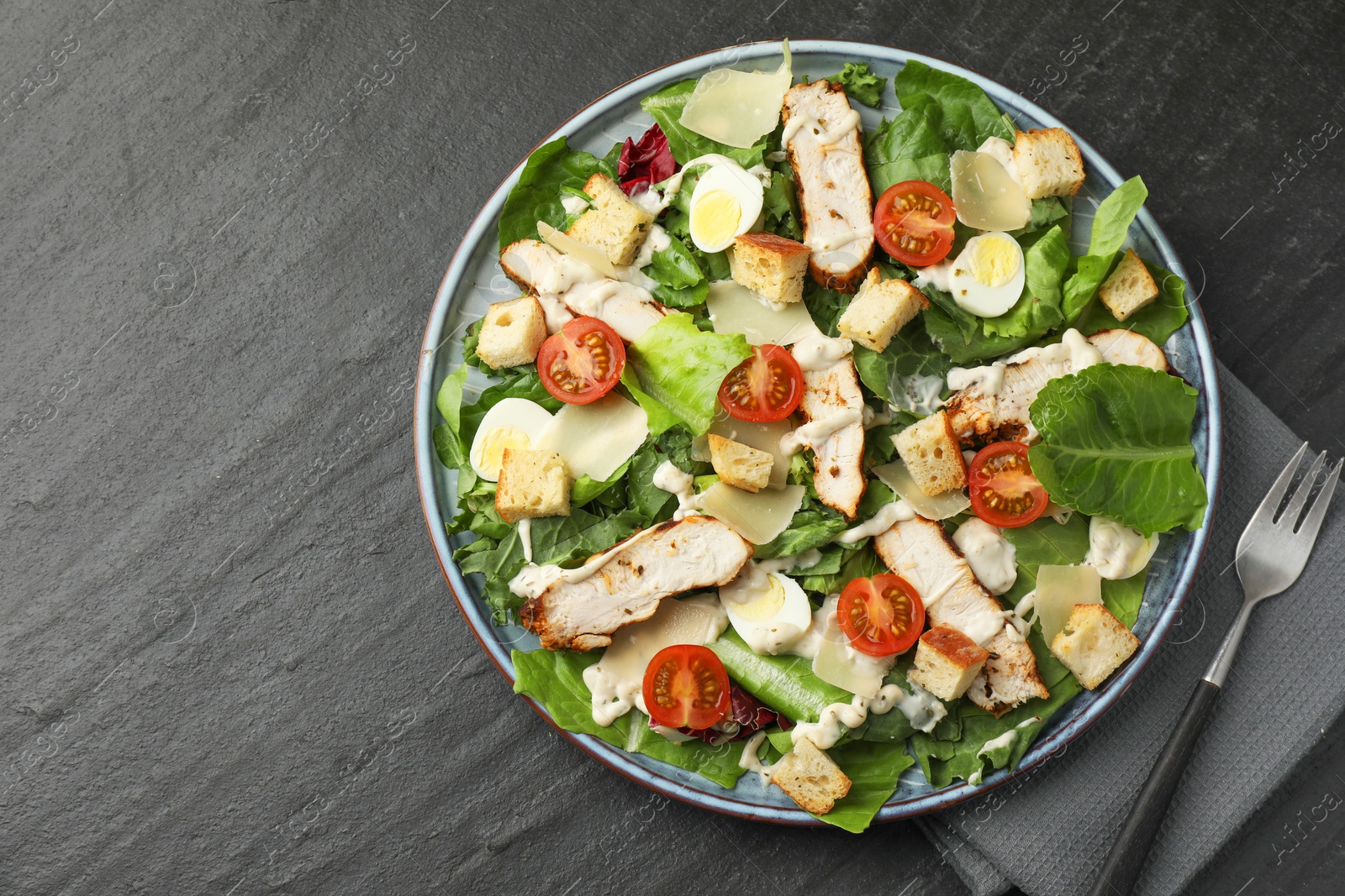 Photo of Tasty Caesar salad with chicken and tomatoes served on dark gray textured table, flat lay. Space for text