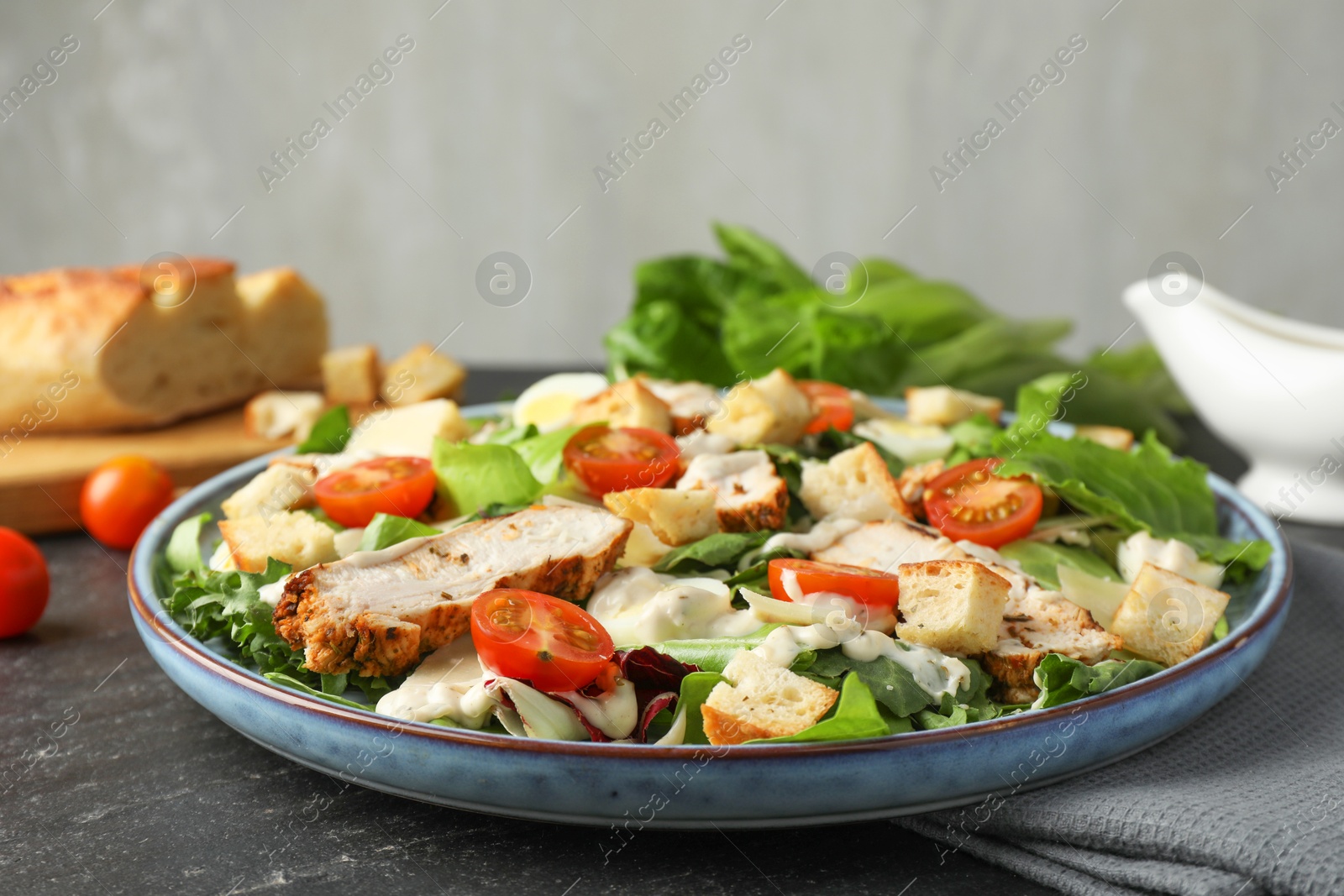 Photo of Tasty Caesar salad with chicken and tomatoes on dark gray textured table, closeup