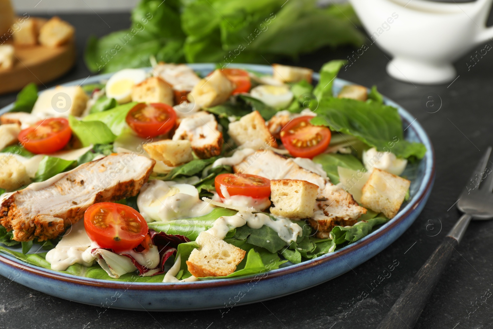 Photo of Tasty Caesar salad with chicken and tomatoes served on dark gray textured table, closeup