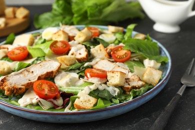 Photo of Tasty Caesar salad with chicken and tomatoes served on dark gray textured table, closeup