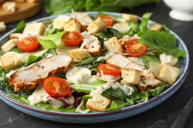 Photo of Tasty Caesar salad with chicken and tomatoes on dark gray textured table, closeup