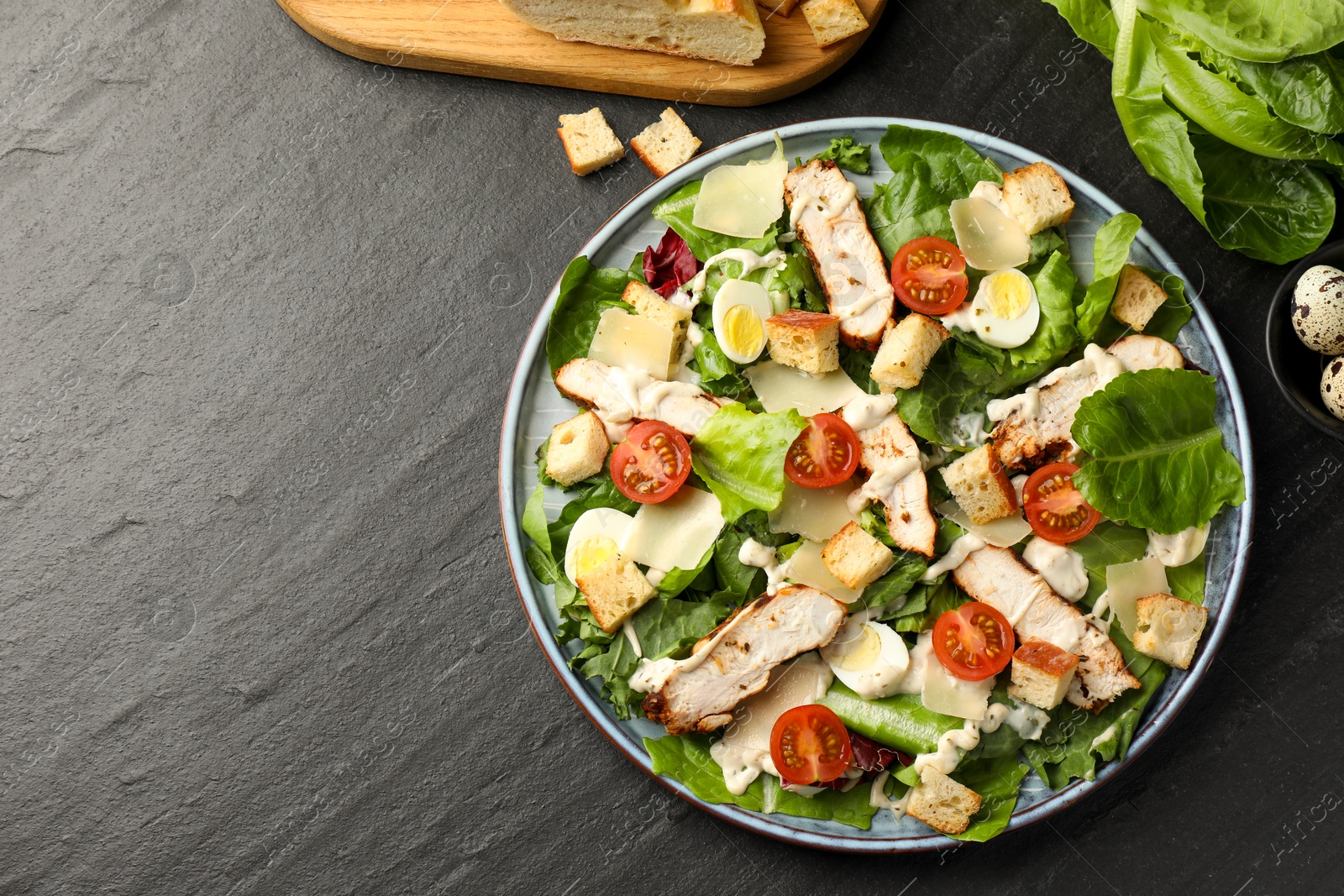 Photo of Tasty Caesar salad with chicken and ingredients on dark gray textured table, flat lay. Space for text