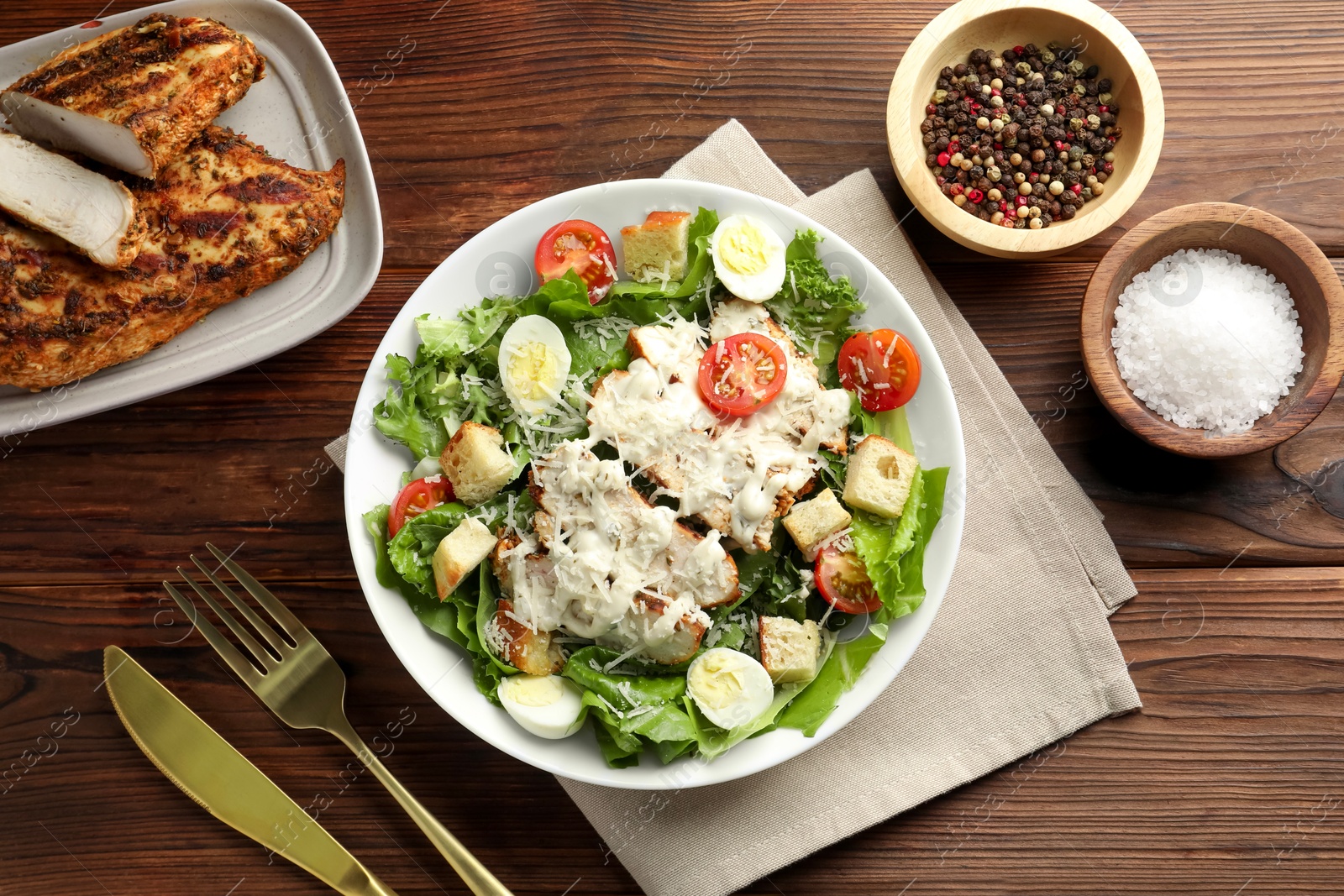 Photo of Tasty Caesar salad with chicken and tomatoes in bowl served on wooden table, flat lay