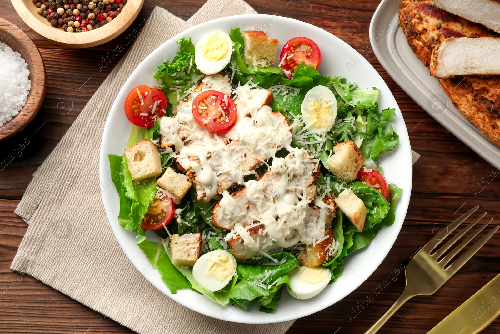 Photo of Tasty Caesar salad with chicken and tomatoes in bowl served on wooden table, flat lay