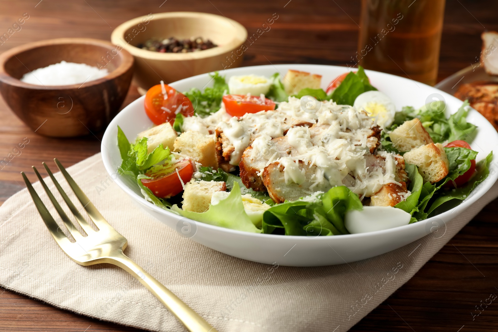 Photo of Tasty Caesar salad with chicken and tomatoes in bowl served on wooden table, closeup