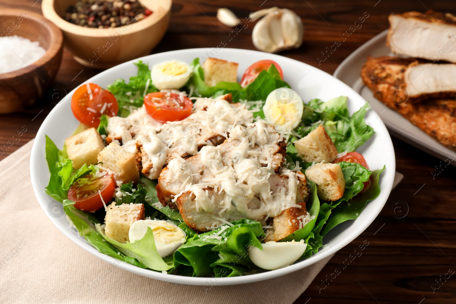 Photo of Tasty Caesar salad with chicken and tomatoes in bowl on wooden table, closeup