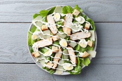 Photo of Delicious Caesar salad with chicken on grey wooden table, top view