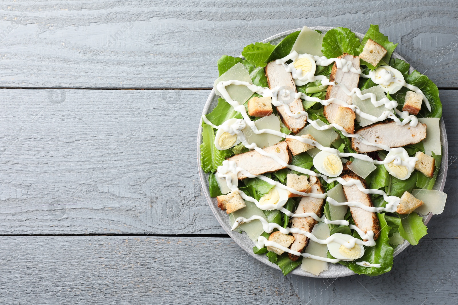 Photo of Delicious Caesar salad with chicken on grey wooden table, top view. Space for text