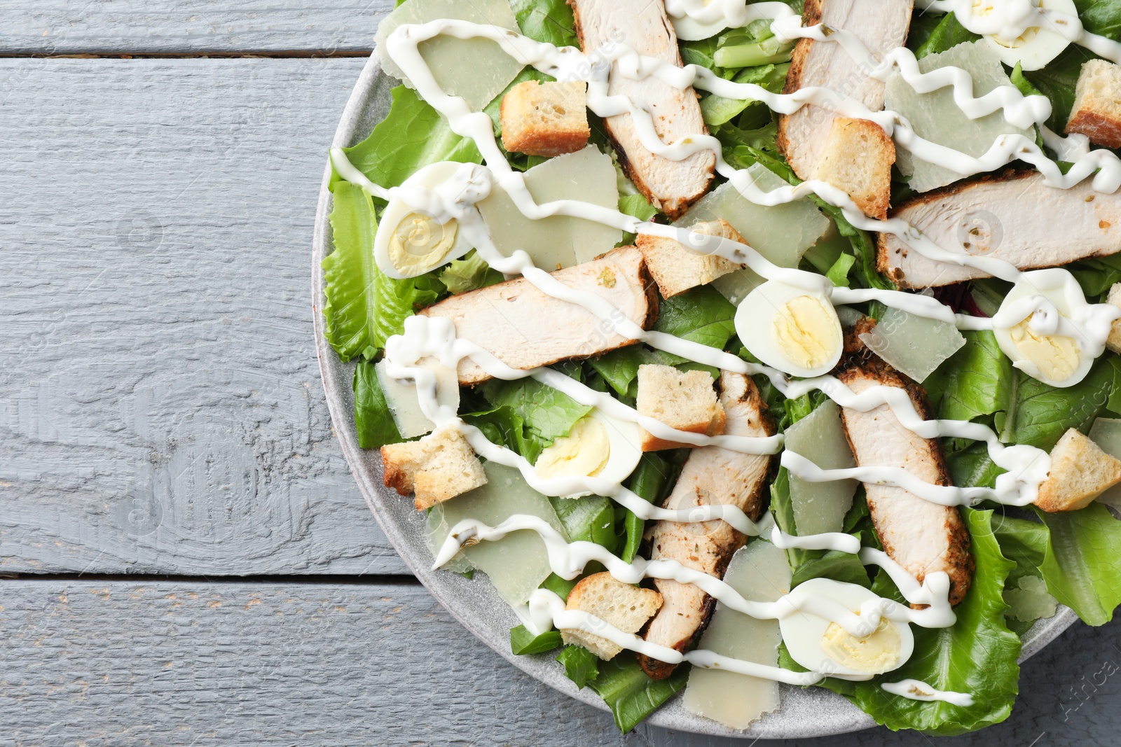 Photo of Delicious Caesar salad with chicken on grey wooden table, top view. Space for text